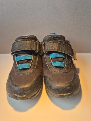 Bruna sneakers med blå detaljer - Snygga bruna sneakers med blå detaljer och kardborreband för enkel påtagning. Skorna har en robust sula och blå meshfoder på insidan samt blåa elastiska band över vristen. Perfekta för en aktiv vardag och passar till många olika stilar. 