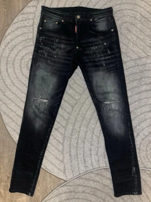 Dsquared2 jeans svarta  - Snygga svarta skinny jeans med slitningar och stänkdetaljer framtill. Jeansen har fem fickor, knappgylf och en smal passform. Perfekta för en trendig och avslappnad stil.