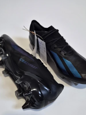 Svarta fotbollsskor med blå detaljer - EU 40 2/3. Helt nya. Sg. Box extra dobbar medkommer.