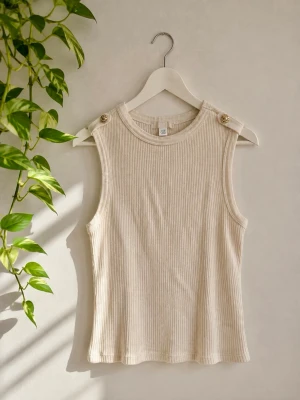 Ribbad beige ärmlös topp med knappar - Snygg ribbad topp i beige med ärmlös design och dekorativa guldfärgade knappar på axlarna. Perfekt till jeans eller kjol för en clean och stilren look.