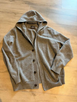 Grå hoodie-kofta från Less Worries - Mysig grå kofta med huva från Less Worries. Koftan har knäppning med mörka knappar, i extremt bra skick knappt använd köpt för 1.2