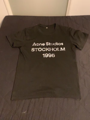 Svart Acne Studios t-shirt - Snygg svart t-shirt från Acne Studios med vit text 'Acne Studios STOCKHOLM 1996' på bröstet. Klassisk passform och rund halsringning, PRIS GÅR O DISKUTERA!