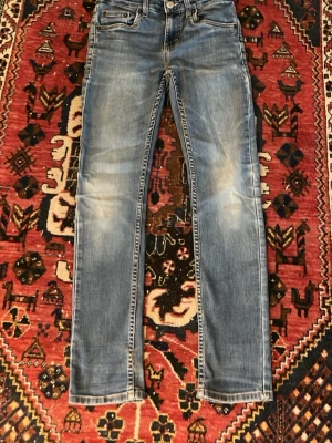 Ljusblå slim fit jeans - Säljer ett par ljusblå slim fit jeans med klassisk femficksdesign och snygga slitningar på framsidan. Jeansen har normal midja och raka ben. Perfekta för en avslappnad och trendig look.