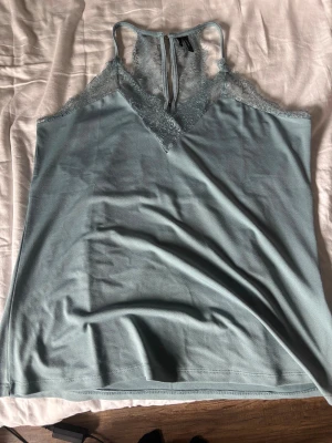 Turkost/mintgrön spetslinnetopp Vero Moda - Supersöt turkost/mintgrön linnetopp från Vero Moda med spetsdetaljer vid halsringningen och axelpartiet. Toppen har v-ringad front och tunna axelband, perfekt för en fräsch och trendig look.