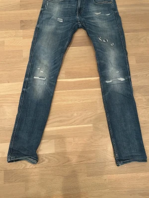 Blå slitna slimfitjeans - Ett par blå slimfitjeans med slitningar och distressed detaljer på både fram- och baksida. Jeansen har klassisk femficksmodell och är tillverkade i denim med lätt tvättad look. Perfekta för en avslappnad och trendig stil. Modell Ambass slimfit. Personen på bilden är 186cm lång. 