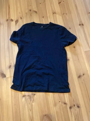 Mörkblå basic t-shirt - En enkel mörkblå t-shirt med rund hals och korta ärmar. Tillverkad i mjuk bomull som känns skön mot huden. Perfekt till jeans eller shorts för en clean och avslappnad stil.från hm aldrig använt