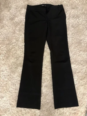 Svarta utsvängda kostymbyxor - Snygga svarta kostymbyxor med utsvängda ben och klassisk passform. Byxorna har hällor för skärp och sidofickor. Perfekta för en stilren look och passar till många olika outfits.