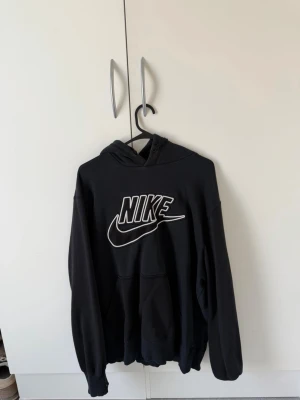 Nike vintage hoodie - Snygg svart hoodie från Nike med stor vit logga och swoosh på bröstet. Klassisk känguruficka framtill och huva med dragsko. Perfekt för en avslappnad och sportig stil. Tillverkad i mjukt material som känns skönt mot huden.