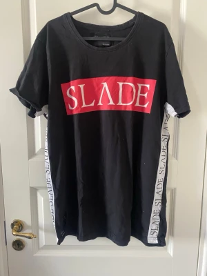 Svart SLÅDE t-shirt med tryck - Svart t-shirt från SLADE med stort rött och vitt tryck framtill och text längs sidorna. Medföljer en likadan i vit också.