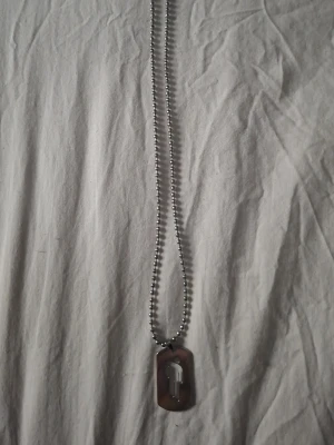 Kedjehalsband med dog tag-hänge - Snyggt halsband med silverfärgad kulkedja och ett dog tag-inspirerat hänge i metall. Hänget har en rektangulär form och en blank yta, vilket ger en cool och stilren look. Perfekt accessoar för dig som gillar minimalistisk och edgy stil.