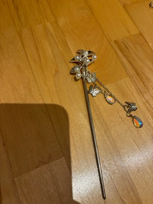 Silverfärgad hårpinne med pärlor - Snygg hårpinne i silverfärg med dekorativa pärlor och löstagbar kedja med fjärilar och regnbågsskimrande droppar. Perfekt för att ge din frisyr en unik och elegant touch. Materialet ser ut att vara metall och plastpärlor.