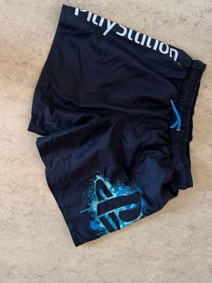 Playstation badshorts  - Jag säljer Playstation badkläder i storlek 164. Mycket bra skick, perfekta för Playstation-fantasten!  *   Storlek: 164 (ca 13-14 år) *   Motiv: Playstation-logotyper *   Skick: Mycket bra *   Material: Snabbtorkande  Pris: 40kr. Intresserad? Kontakta mig här!