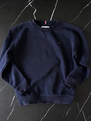 Tommy Hilfiger sweatshirt – marinblå, strl 140cm - Snygg och klassisk Tommy Hilfiger sweatshirt i tidlös marinblå färg 💙 Perfekt för skolan, vardagen eller som ett extra lager under kyligare dagar. ✨ Storlek: 140 cm, ca 9–10 år ✨ Färg: Marinblå / navy blue ✨ Material: Mjuk och bekväm bomull ✨ Passform: Klassisk modell som är enkel att matcha med jeans, chinos eller mjukisbyxor ✨ Skick: Mycket fint skick – inga fläckar, hål eller andra anmärkningar Ett stilrent och lättmatchat märkesplagg som passar säsong efter säsong. Perfekt för dig 