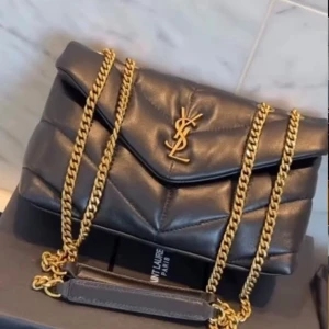 Svart YSL handväska med guldkedja - Säljer en svart quiltad handväska från Saint Laurent med ikonisk YSL-logga i guld framtill. Väskan har en lyxig guldfärgad kedjerem och är tillverkad i mjukt läder. Perfekt accessoar för att lyfta vilken outfit som helst.