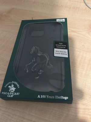 Mobilskal Santa Barbara Polo i svart - Snyggt svart mobilskal från Santa Barbara Polo & Racquet Club med hästmotiv. Skalets material ger en mjuk känsla och har hög temperaturresistens. Passar iPhone 14 Pro Max och har en stilren design med exklusiv känsla.