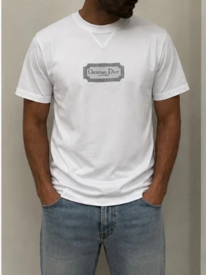 Vit  t-shirt - Snygg vit t-shirt  med grå logga på bröstet. Klassisk rund halsringning och korta ärmar. Tillverkad i mjuk bomull för en skön känsla och stilren look. Perfekt till jeans eller shorts för en clean outfit.