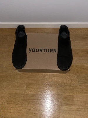 Svarta Chelsea boots från Yourturn - Säljer ett par stilrena svarta Chelsea boots från Yourturn. Skorna har klassisk resår på sidorna och är tillverkade i mockaimitation. Perfekta för dig som vill ha en clean och tidlös look till hösten och vintern.