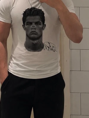 CR7 Vit t-shirt storlek m - Säljer en vit CR7 t-shirt med ett stort svartvitt porträtt och signatur på framsidan. Baksidan har ett grafiskt tryck med texten 'CUZ ANYTHING IS YOURS'. T-shirten har korta armar och normal passform. Perfekt för dig som gillar unika prints och streetwear.