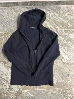 Mörkblå hoodie från Lawrence Grey - Snygg mörkblå hoodie från Lawrence Grey med dragkedja framtill och huva. Tillverkad i ett mjukt, stickat material som känns riktigt skönt mot huden. Perfekt för dig som gillar en enkel men stilren look. Långa ärmar och ribbade muddar.