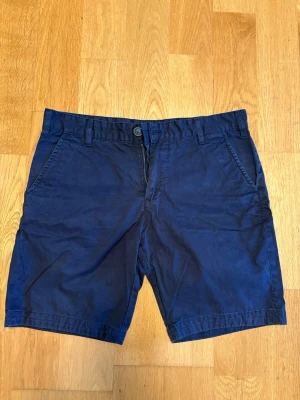 Mörkblå bomullsshorts med fickor - Snygga mörkblå shorts i klassisk passform. Shortsen har sidofickor, bälteshällor och två bakfickor. Perfekta för varma dagar och enkla att matcha med olika stilar.