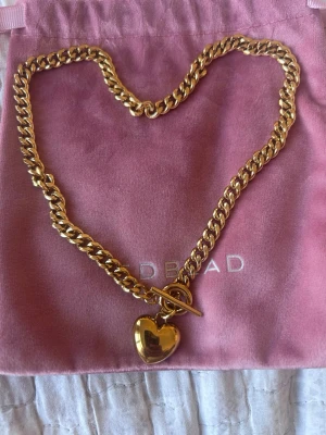 Edblad halsband med hjärthänge - Pansarkedja med ett stort fylligt hjärta i t-låset, i blank rostfritt stål med 14K guldplätering från Edblad. Material: Rostfritt stål med 14K guldplätering Mått: 20 x 18 mm Kedjans längd 45 cm Material: Rostfritt stål med 14K guldplätering 