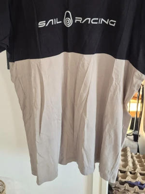 Sail Racing tvåfärgad t-shirt - T-shirt från Sail Racing med svart överdel och beige nedtill. Klassisk passform och korta ärmar. Stor logga framtill. Perfekt för en avslappnad och sportig stil.