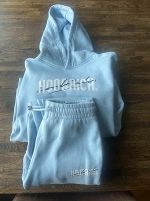 Ljusblå hoodiedress från Hoodrich 12-13år - Snygg ljusblå hoodiedress från Hoodrich med stor vit logga framtill. Klassisk huva och magficka, ribbade muddar vid ärmar och nederkant. 