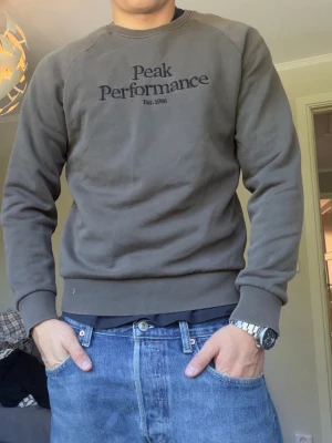 Olivgrön sweatshirt Peak Performance - Säljer en olivgrön sweatshirt från Peak Performance med broderad logga på bröstet. Tröjan har rund halsringning, ribbade muddar vid ärmslut och nederkant samt en avslappnad passform. Perfekt för en casual look.