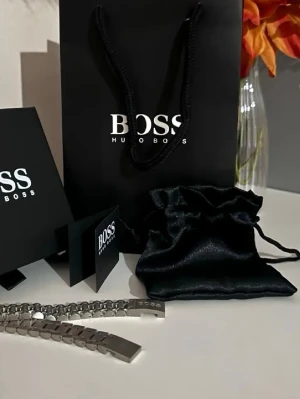 Silverfärgad länkarmband från BOSS - Snyggt och stilrent silverfärgat länkarmband från BOSS, perfekt som extra armband till din klocka. Tillverkad i metall med klassisk design och BOSS-logga på spännet. Kommer med originalpåse och förpackning.