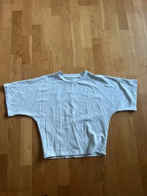 Ljusgrå t-shirt med breda ärmar - En ljusgrå t-shirt i bomull med breda, korta ärmar och loose passform i armarna och över bröstet, ner till magen är den tajtare. T-shirten har rund halsringning och enkel design utan tryck eller mönster. Perfekt för en avslappnad stil. Jätte bra material 