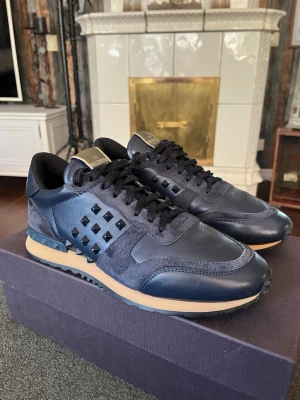 Helt nya Valentino Garavani Rockrunners | Storlek 41 - Snygga mörkblå sneakers med svarta nitar på sidorna och detaljer i mocka och läder. Skorna har svarta skosnören, beige sula och coola pyramidformade detaljer vid hälen. Självklart äkta, original box medföljer inte, nypris ca 5k! 