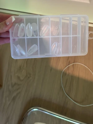 Klara långa press-on naglar i ask - Säljer ett set med långa, klara press-on naglar i en praktisk plastask med flera fack. Naglarna har en elegant almondform och är gjorda av tålig plast, perfekta för att skapa egna designer eller använda som de är.