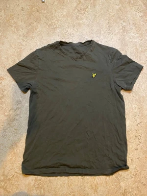 Lyle & Scott grön tshirt - En enkel mörkgrön t-shirt med rund hals och korta ärmar. På bröstet finns en liten gul broderad logga som detalj. Perfekt basplagg till garderoben och tillverkad i mjukt bomullsmaterial.