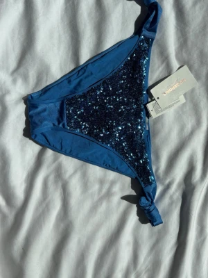 Blå bikiniunderdel med paljetter Calzedonia - Snygg blå bikiniunderdel från Calzedonia med glittriga paljetter framtill och knyt i sidorna. Perfekt för sommaren eller semester. Materialet känns mjukt och stretchigt och den sitter jättefint på. Denna design är limeted edition och säljs inte längre. Helt ny med prislapp.