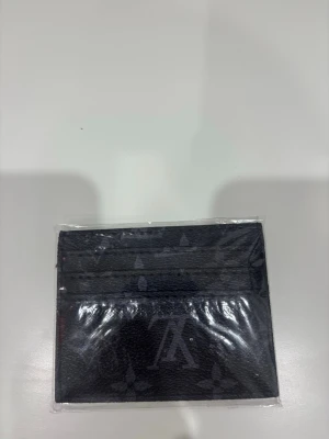 Monogram korthållare  - Snyggt svart kortfodral i läderimitation med diskret monogrammönster. Fodralet har flera kortfack på båda sidor och en stilren, minimalistisk design som passar perfekt i fickan. Perfekt för dig som vill ha koll på korten utan att ta plats.