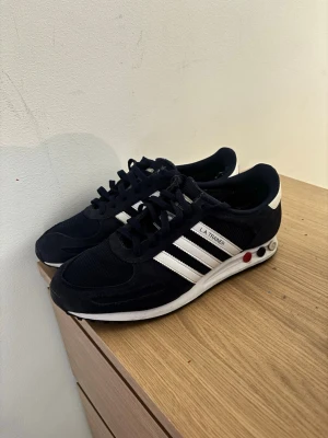 Adidas LA Trainer Blåa - Mörkblåa Adidas La Trainers i fint skick. Allt är som nytt förutom en slitning vid hälen på både skorna, se bild. Priser är inte hugget i sten! Storlek 46