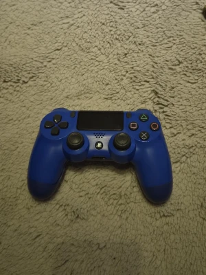Ps4 kontroll - Snygg blå PS4 handkontroll med klassisk layout, två analoga spakar, styrkors och de ikoniska PlayStation-knapparna i färg. Tillverkad i plast med en matt finish och touchpad i mitten. Perfekt för gaming och multiplayer-sessioner.