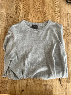 Ljusgrå stickad tröja  - Säljer en tunn ljusgrå stickad tröja från H&M i slim fit-modell. Tröjan har rund halsringning och ribbade muddar vid hals, ärmslut och nederkant. 