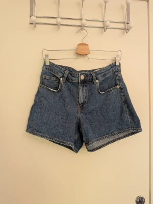 Blå denimshorts med hög midja - Klassiska blå jeansshorts i denim i midrise med något längre ben. Shortsen är från Vero Moda i storlek S.