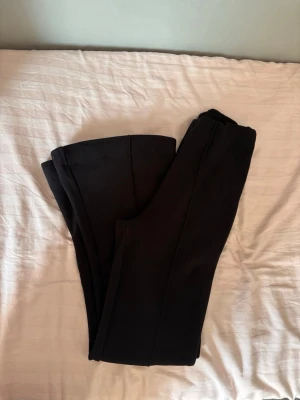 Svarta ribbade leggings - Säljer ett par svarta leggings med ribbad struktur och hög midja. De är stretchiga och mjuka, perfekta för en avslappnad och trendig look. Passar till både oversized tröjor och crop tops. Materialet känns bekvämt och följsamt. observera att byxorna är några cm uppsydda vilket man enkelt kan sprätta upp om man önskar  
