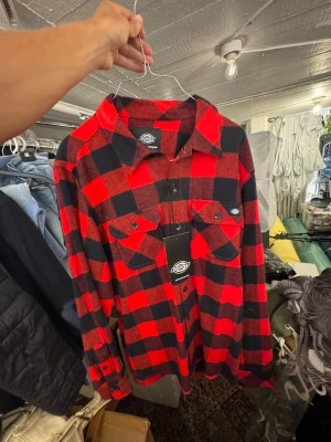 Röd och svart rutig skjorta Dickies - Klassisk röd och svart rutig skjorta från Dickies i mjukt material. Skjortan har två bröstfickor med knappar och lång ärm. Perfekt för dig som gillar en avslappnad och tidlös stil. Finns att hämta i Gröndal. Nypris är 699kr.