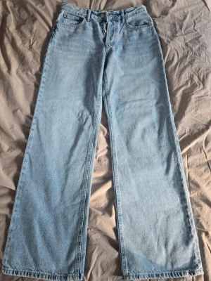 Ljusblåa vida jeans med hög midja - Säljer ett par ljusblå, raka, mid waist jeans och helt nya utan prislapp. Klassisk femficksmodell, passar dig som gillar loose fit och retrostil.