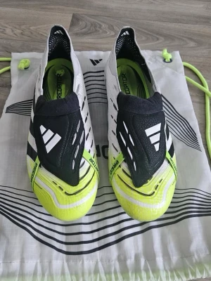 Adidas Predator fotbollsskor gul/svart - Säljer ett par Adidas Predator fotbollsskor i en snygg kombination av vitt, svart och neon-gult. Skorna har låg profil, snörningsfri design och mönstrad ovandel för bättre bollkontroll. Perfekta för dig som vill sticka ut på planen. Helt nya typ använda bara fåtal gånger och köpte dem för 2500. De är elite✅ kan alltid diskutera!