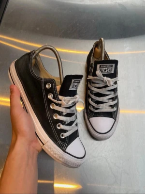 Svarta Converse All Star sneakers - Klassiska svarta Converse All Star sneakers med vit tå och sula. Skorna har snörning, vita sömmar och metallhål för snören. Perfekta för en avslappnad och cool stil.