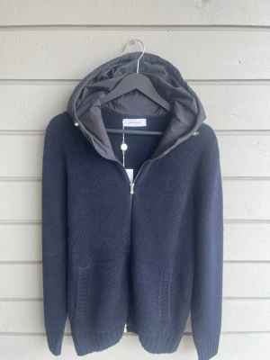 Gran sasso Cardigan ny - Snygg mörkblå hoodie från Gran Sasso med dragkedja framtill och två fickor, helt ny!. Tillverkad i ett mjukt, stickat material och har en vadderad huva som ger extra stilpoäng. Perfekt för dig som vill ha en clean och modern look.