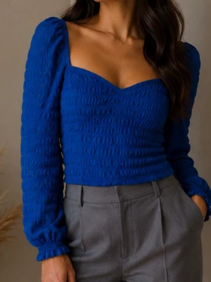 Kornblå långärmad topp med puffärm strl L - Trendig kornblå topp med lång puffärm och smockad struktur. Djup v-ringning och figurnära passform ger en snygg siluett. Perfekt att styla med både jeans och kjol för en cool look.