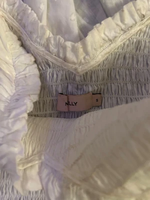 Vit volangklänning från NLY - Supersöt vit kortklänning från NLY med offshoulder och volangdetaljer. Klänningen har smockad överdel och dubbla volanglager i kjolen. Perfekt för sommarens alla tillfällen och ger en romantisk vibe. Tillverkad i mjuk bomull. jag hade den här klänningen på min studentdag jättefin och perfekt