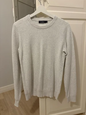 Vi stickad tröja Dressmann - Vit stickad tröja från Dressmann med rund halsringning och diskret strukturmönster. Tröjan har långa ärmar och ribbade muddar vid ärmslut och nederkant. Perfekt för lager-på-lager och enkel att matcha med olika outfits.