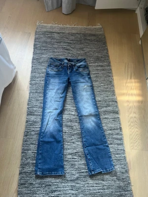 Blå bootcut jeans från LTB - Säljer ett par blå bootcut jeans från LTB, modell Valerie. Jeansen har en snygg tvätt med slitningar och ljusare partier på låren och knäna. Klassisk femficksmodell med knapp- och dragkedjegylf. Perfekta för en avslappnad och trendig look.
