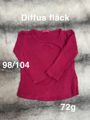 Mörkrosa långärmad topp med rosett - Mörkrosa långärmad topp med liten rosettdetalj framtill. Enkel och mjuk design, perfekt till vardags. Rund halsringning och normal passform.🌸Diffusa fläckar. Storlek 98/104 